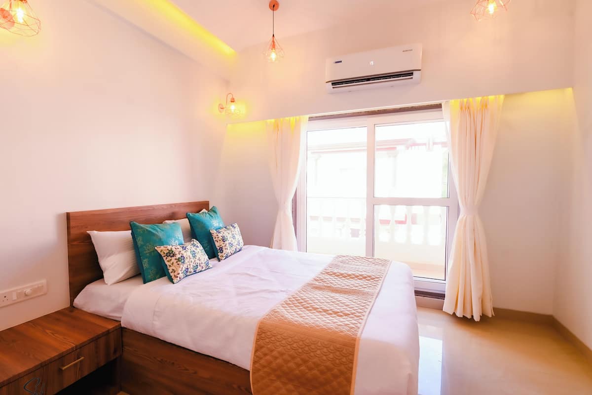 A bedroom with a wooden headboard, a bed with white bedding and decorative pillows, a bedside table, and a window with curtains.