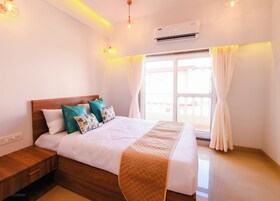 Un dormitorio con cabecera de madera, una cama con ropa de cama blanca y almohadas decorativas, una mesita de noche y una ventana con cortinas.