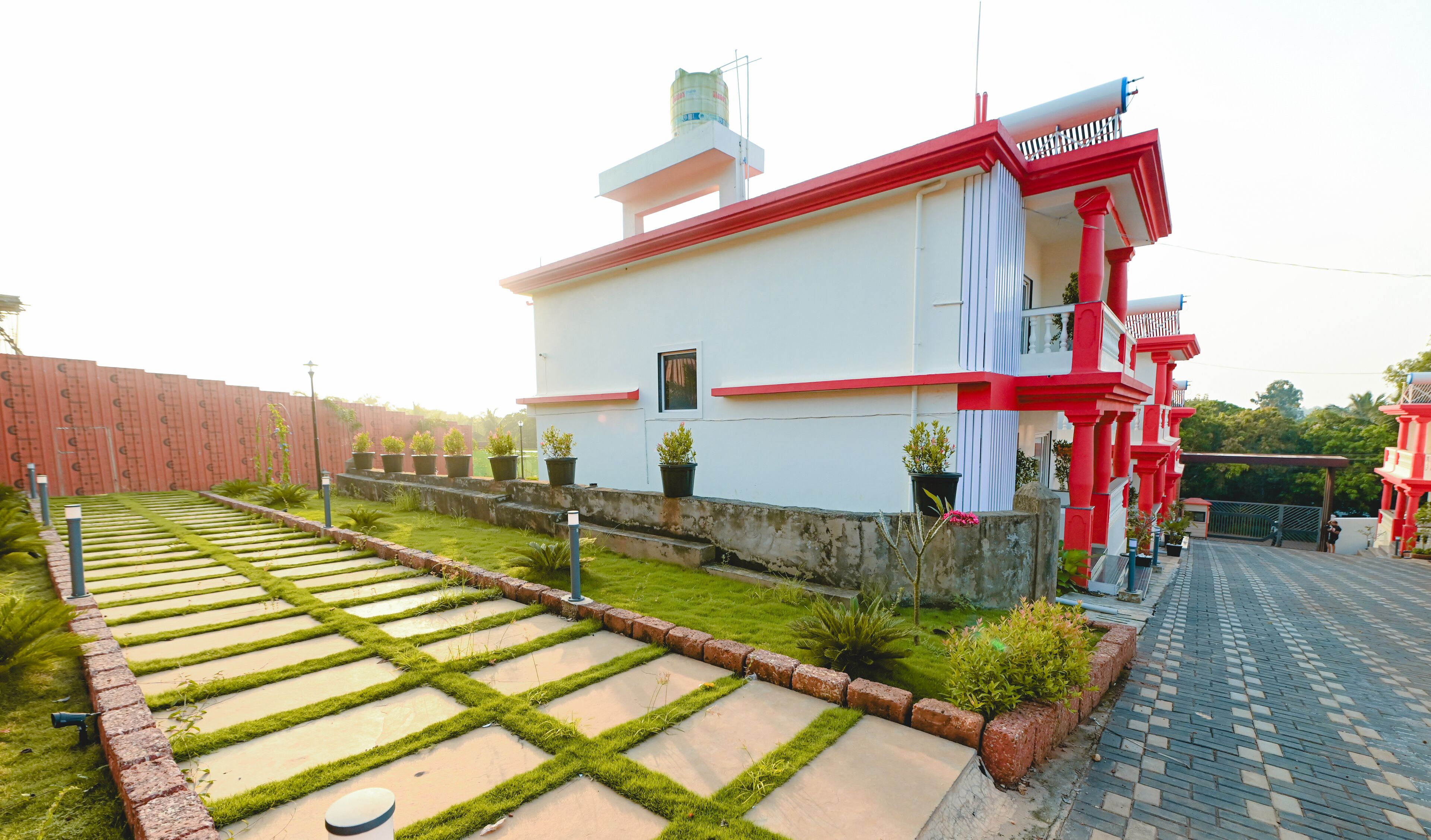 Ein Gebäude mit roter und weißer Fassade, ein gepflasterter Garten mit trittfesten Steinen und ein kleines Fenster.