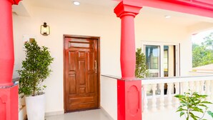 A building entrance with a wooden door, red columns, and potted plants.