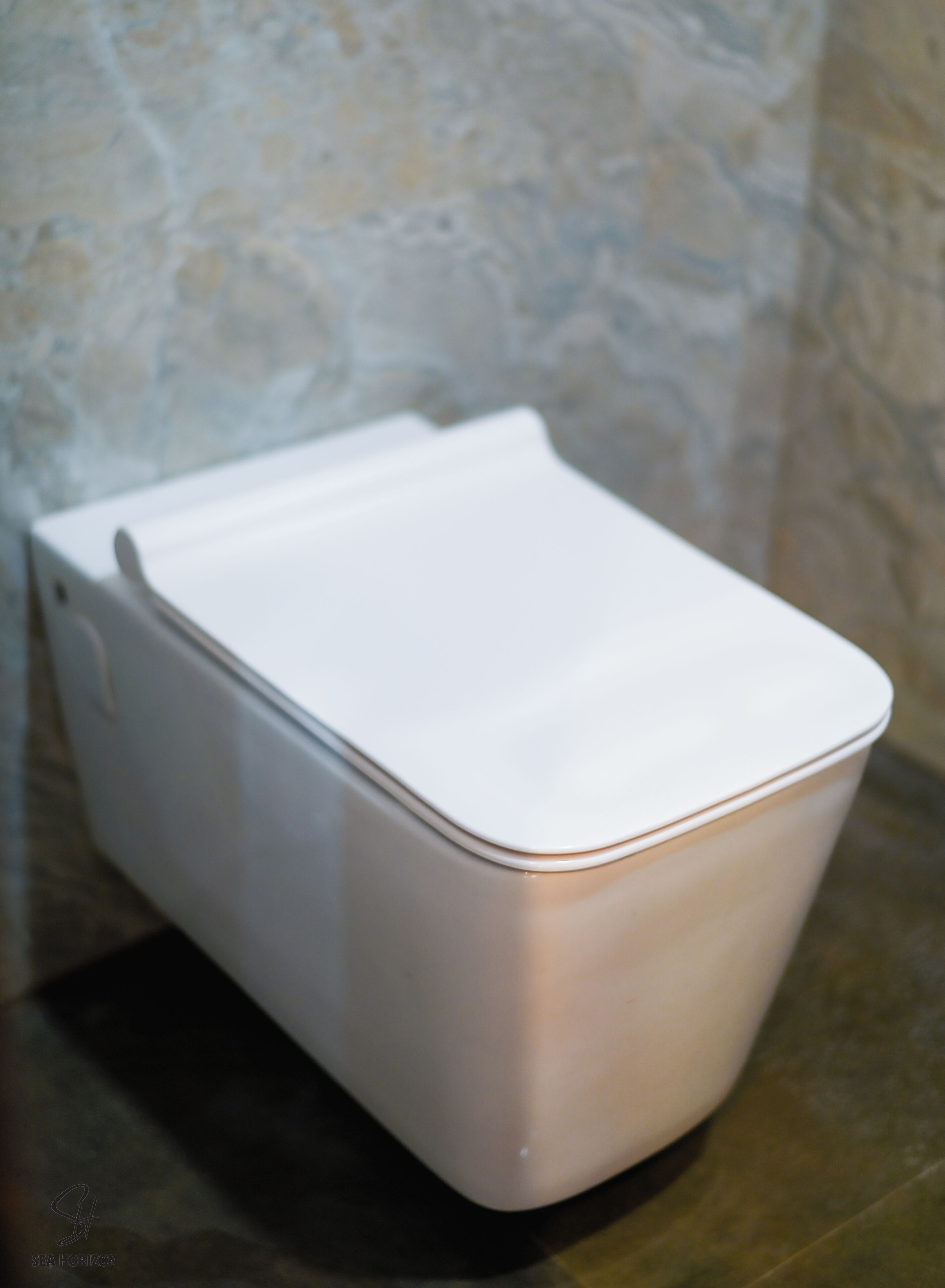 A white, rectangular, metallic object with a curved top, likely a piece of furniture, against a textured wall.