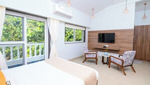 A hotel room with a bed, two chairs, a TV, and large windows with a view of greenery.