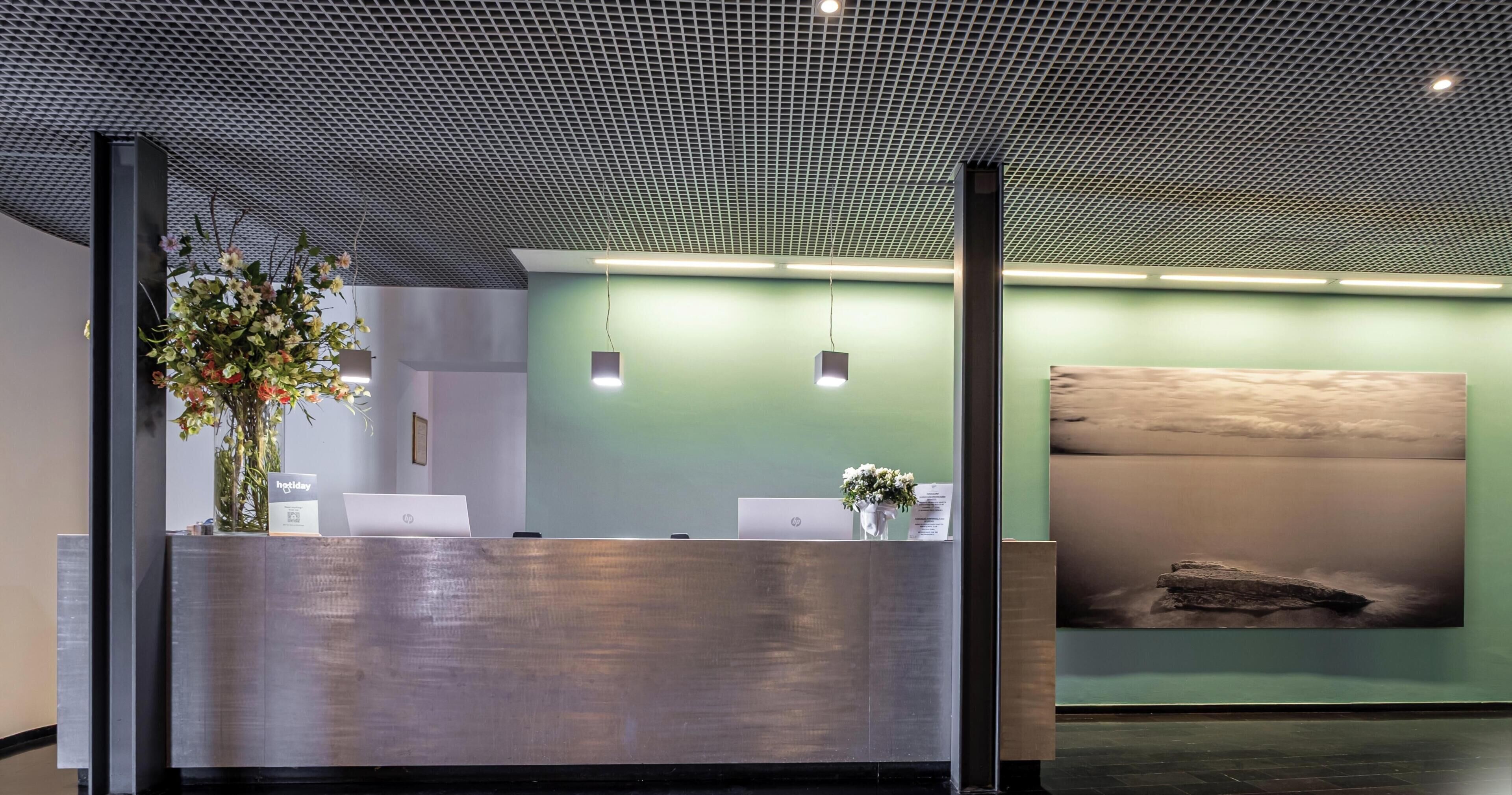 A reception area with a modern design, featuring a metal reception desk, a green wall, and a large abstract painting.