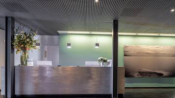 A reception area with a modern design, featuring a metal reception desk, a green wall, and a large abstract painting.