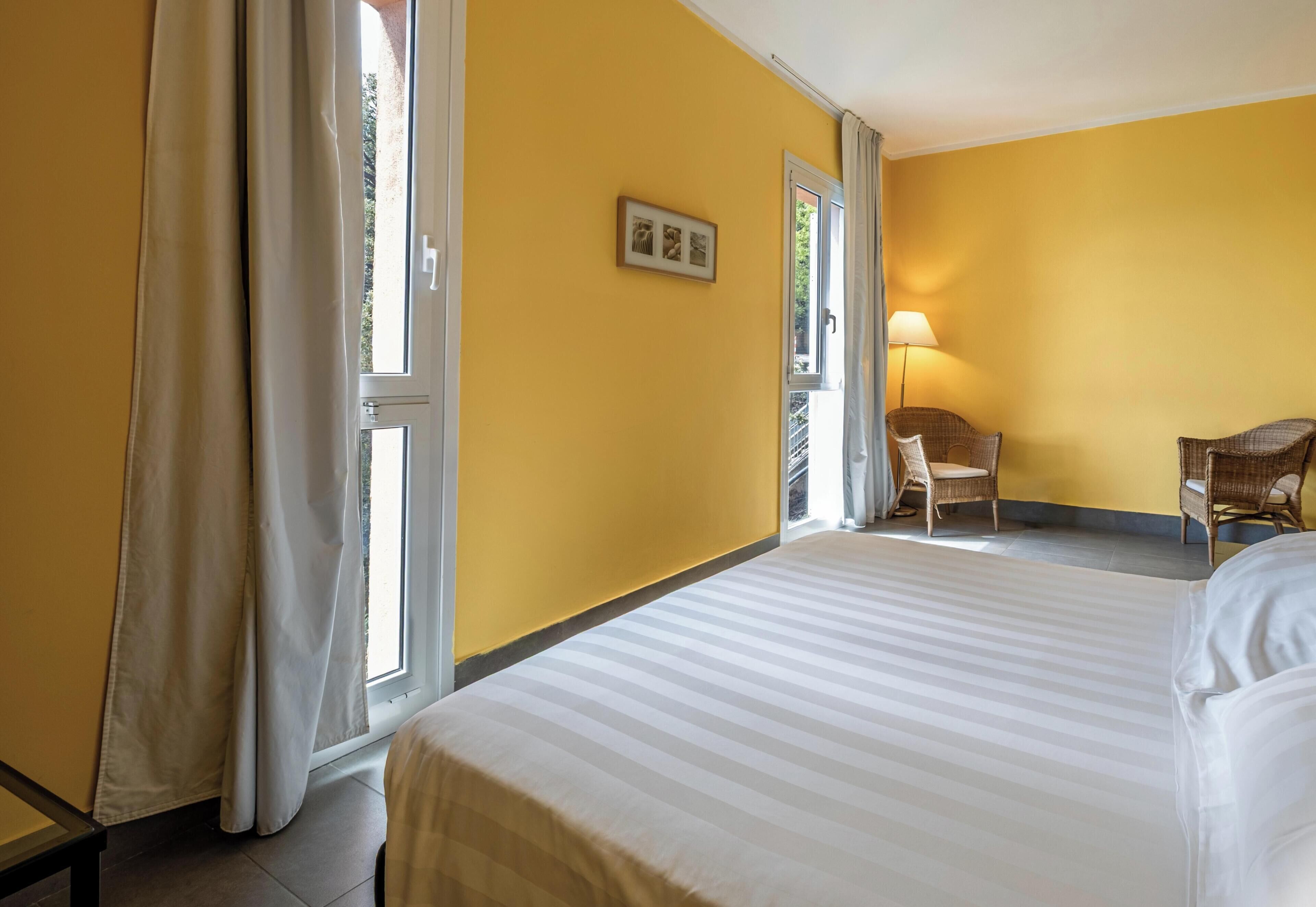 A hotel room with a bed, a chair, a lamp, and a window with curtains.