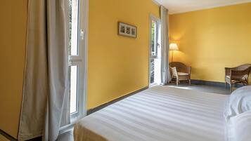 A hotel room with a bed, a chair, a lamp, and a window with curtains.