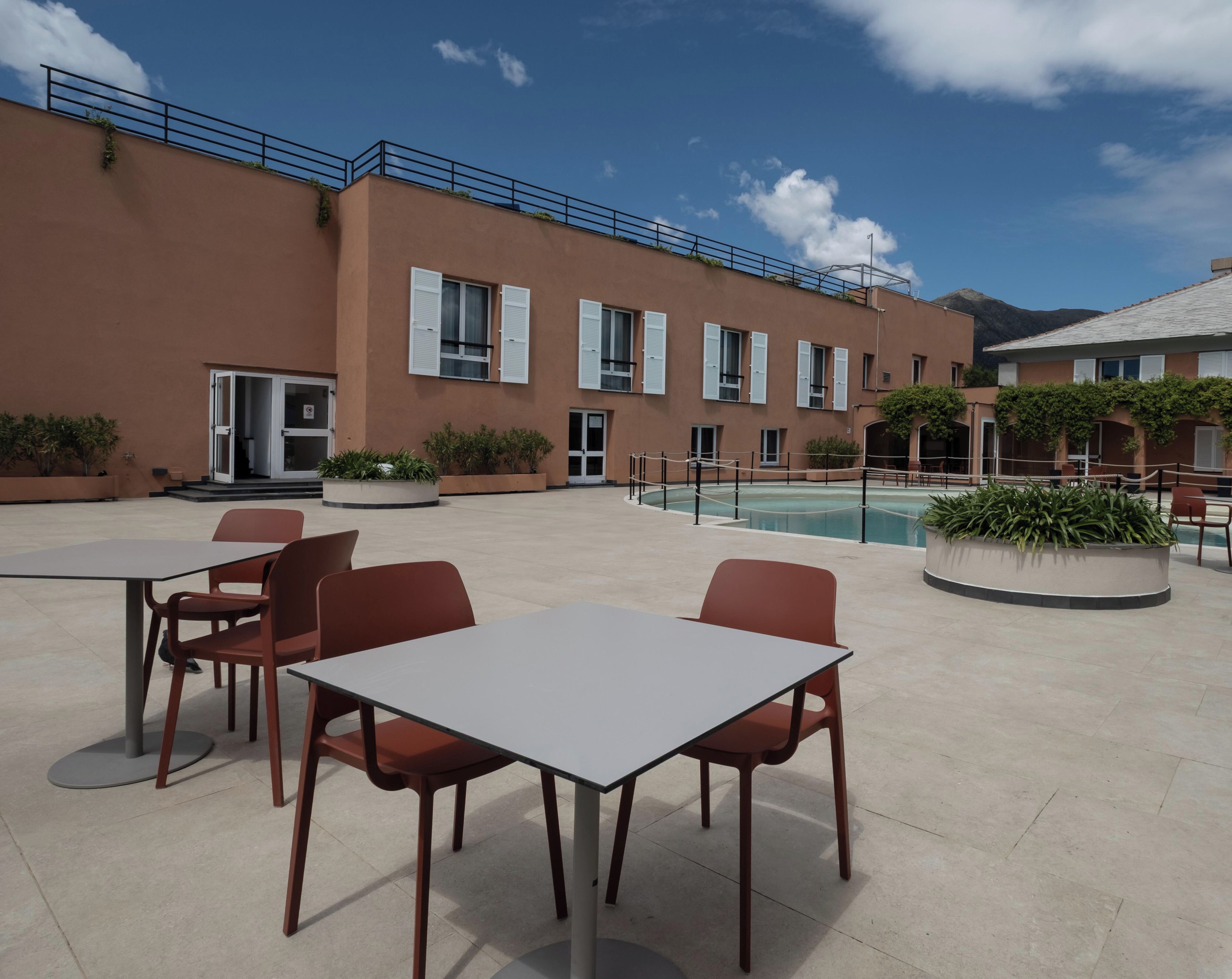 An outdoor seating area with tables and chairs, a pool, and a building with windows and a balcony.