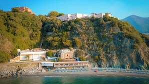 A coastal hotel with multiple buildings on a hillside, a beach with sun loungers, and clear blue waters. - Hotiday Arenzano Pineta (Arenzano)