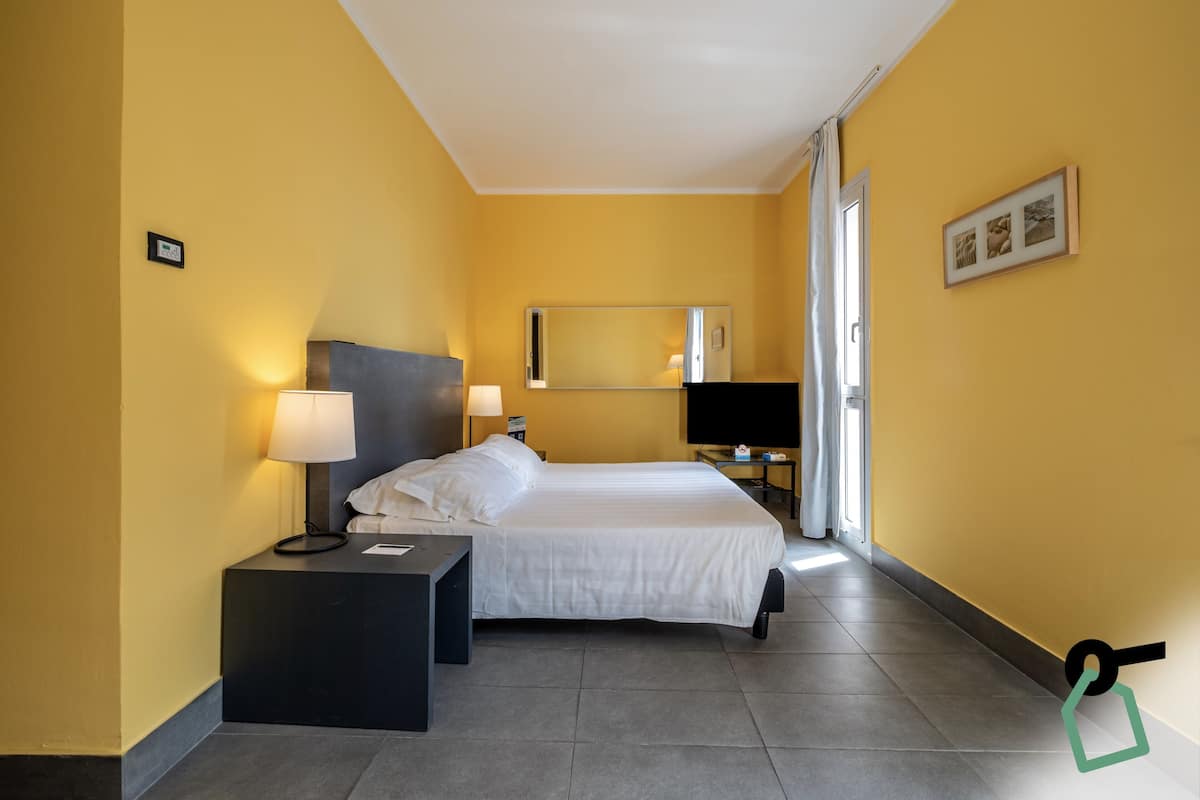 A hotel room with a bed, bedside tables, a TV, and a mirror.