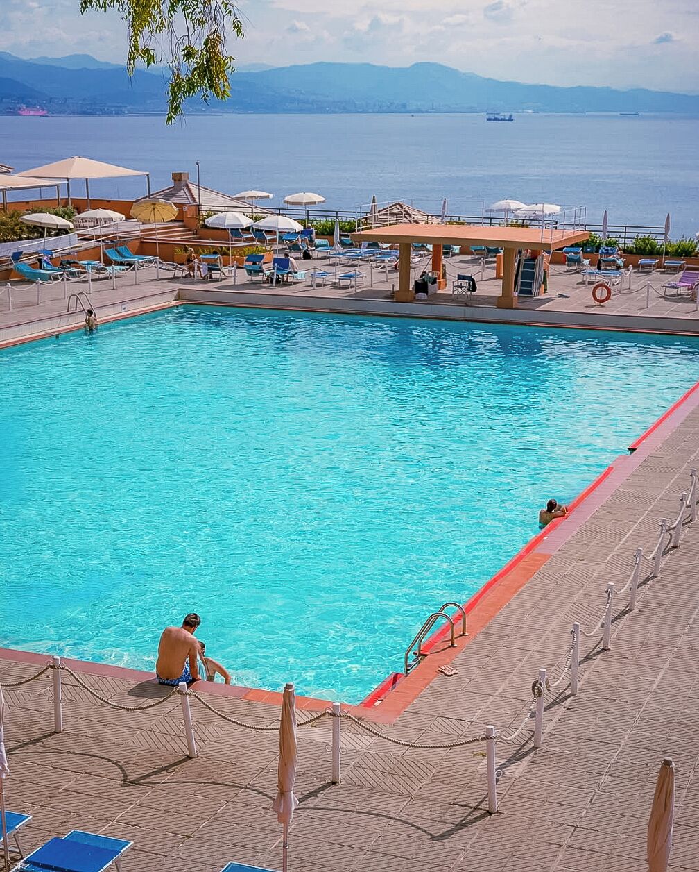 A swimming pool with a view of the sea, sun loungers, and a covered seating area.