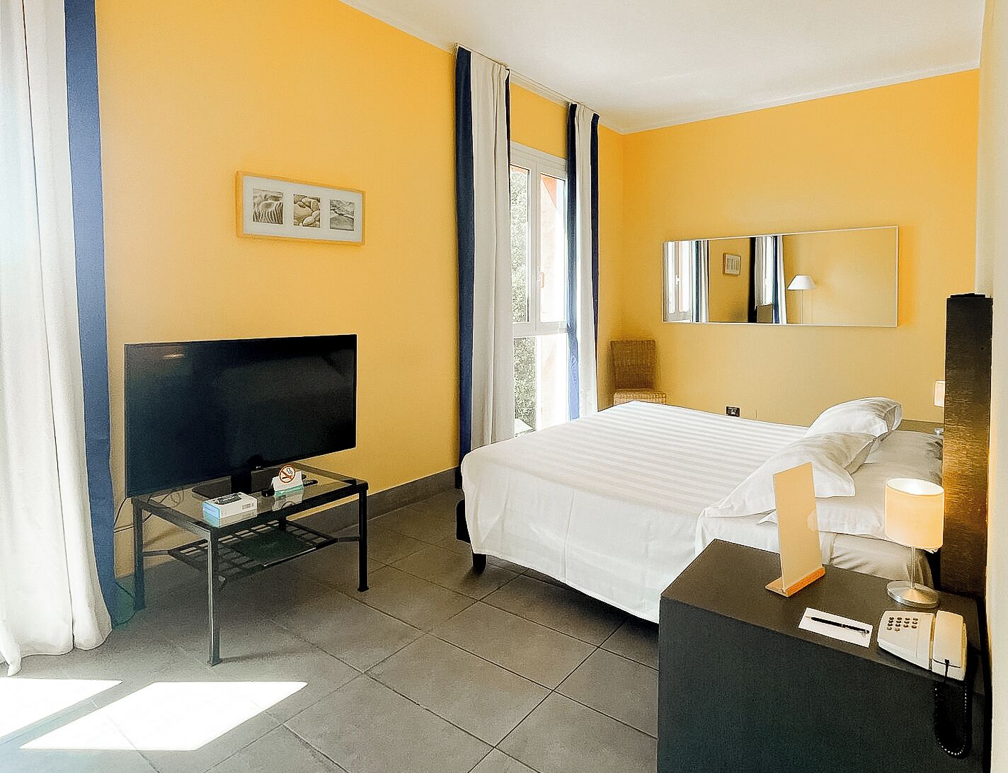A hotel room with a bed, a TV, a desk with a phone, and a mirror.