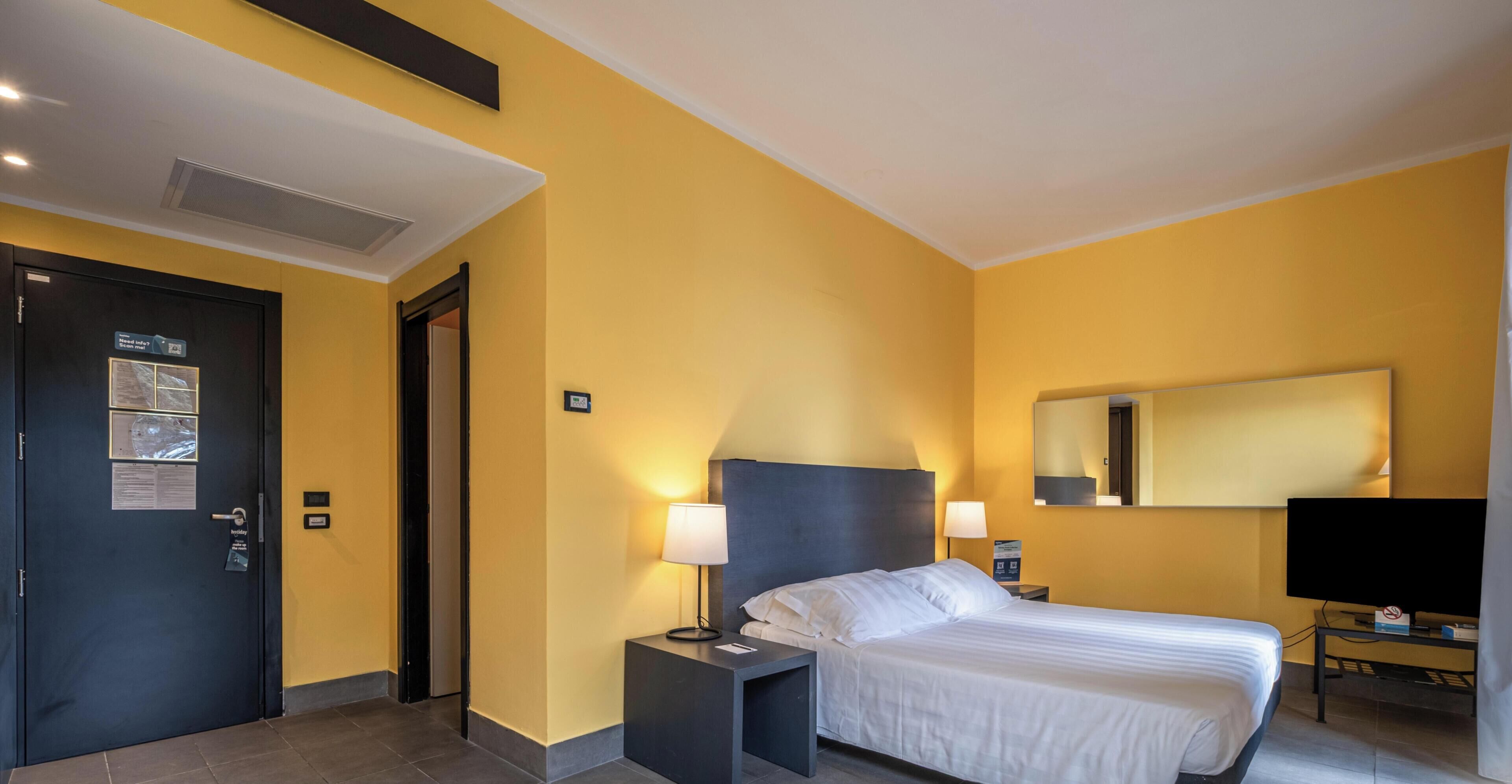 A hotel room with a bed, bedside tables, a mirror, and a television.