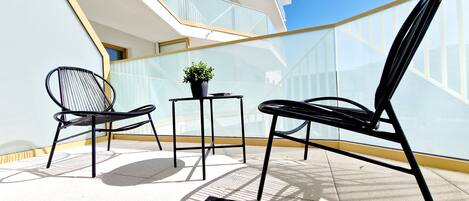 Een balkon met twee zwarte stoelen, een tafeltje met een plant in pot, en een deurmat.