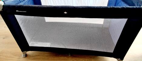 A portable crib with a mesh side and a white mattress, placed on a wooden floor.