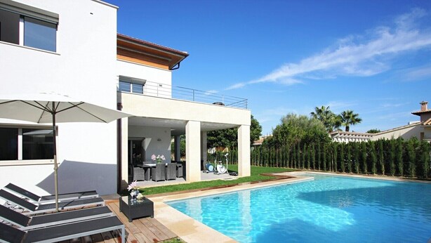 Una casa moderna con piscina, mobiliario exterior y un patio cubierto.