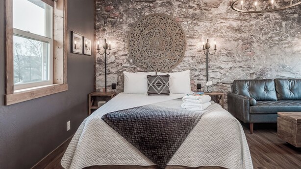 Ein Schlafzimmer mit einem großen Bett, einer Steinwand, einer Chandelier und einem Ledersofa.
