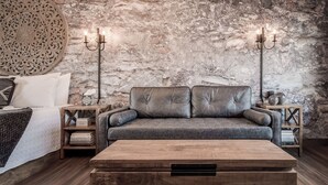 Ein gemütliches Wohnzimmer mit Steinwand, grauem Sofa, Couchtisch aus Holz und zwei Nachttischen mit Lampen.