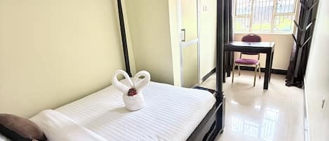A room with a four-poster bed, a small table with a chair, and a window with curtains.