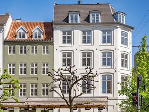 Uma fileira de edifícios de vários andares com estilos arquitetônicos distintos, incluindo um edifício com fachada verde e um prédio branco com janelas salientes.