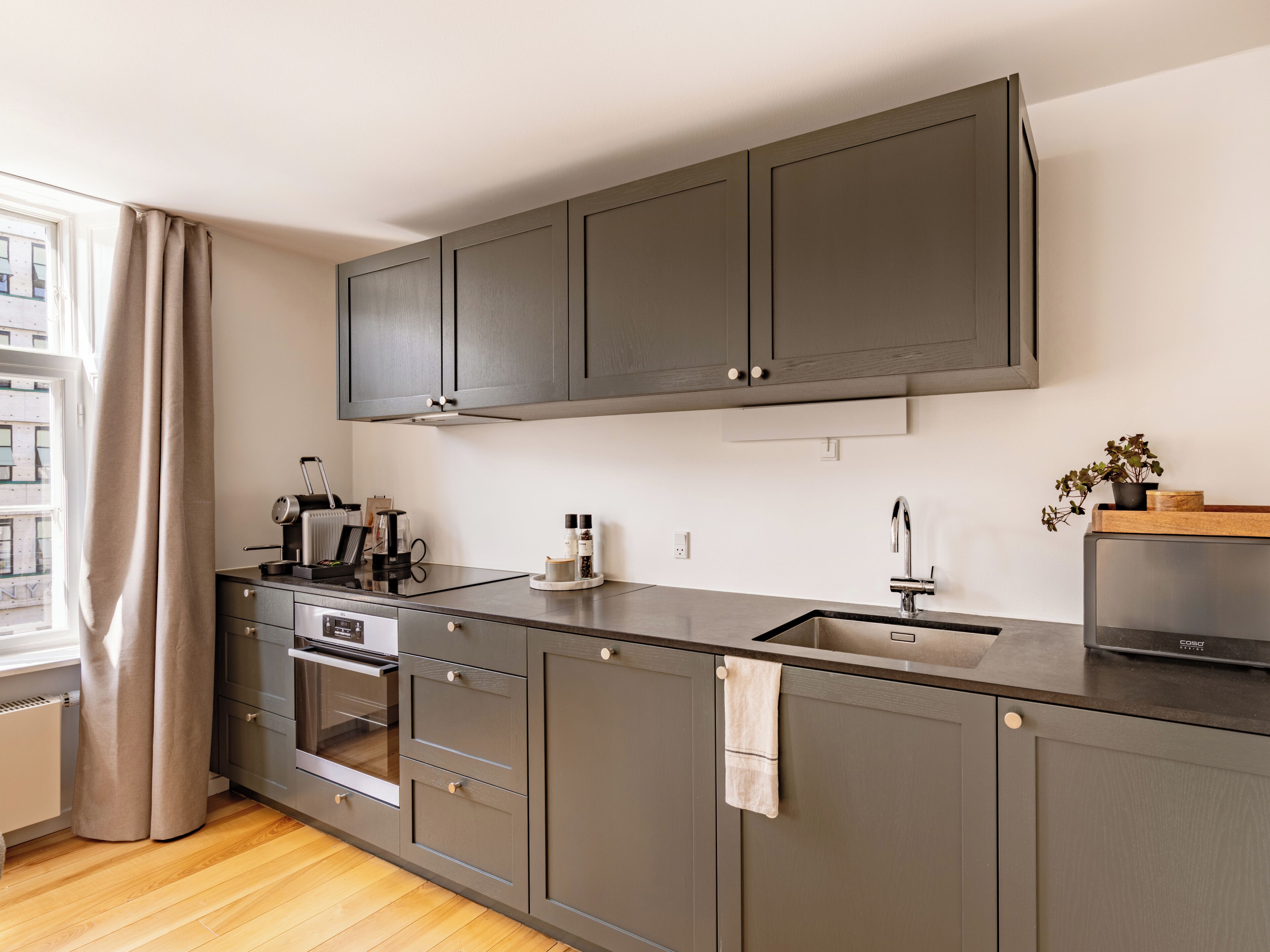 A modern kitchen with grey cabinets, a built-in oven, and a stainless steel sink.