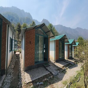 Una hilera de pequeñas casas de huéspedes modernas, con paredes de ladrillo y amplias ventanas, frente a un paisaje montañoso.
