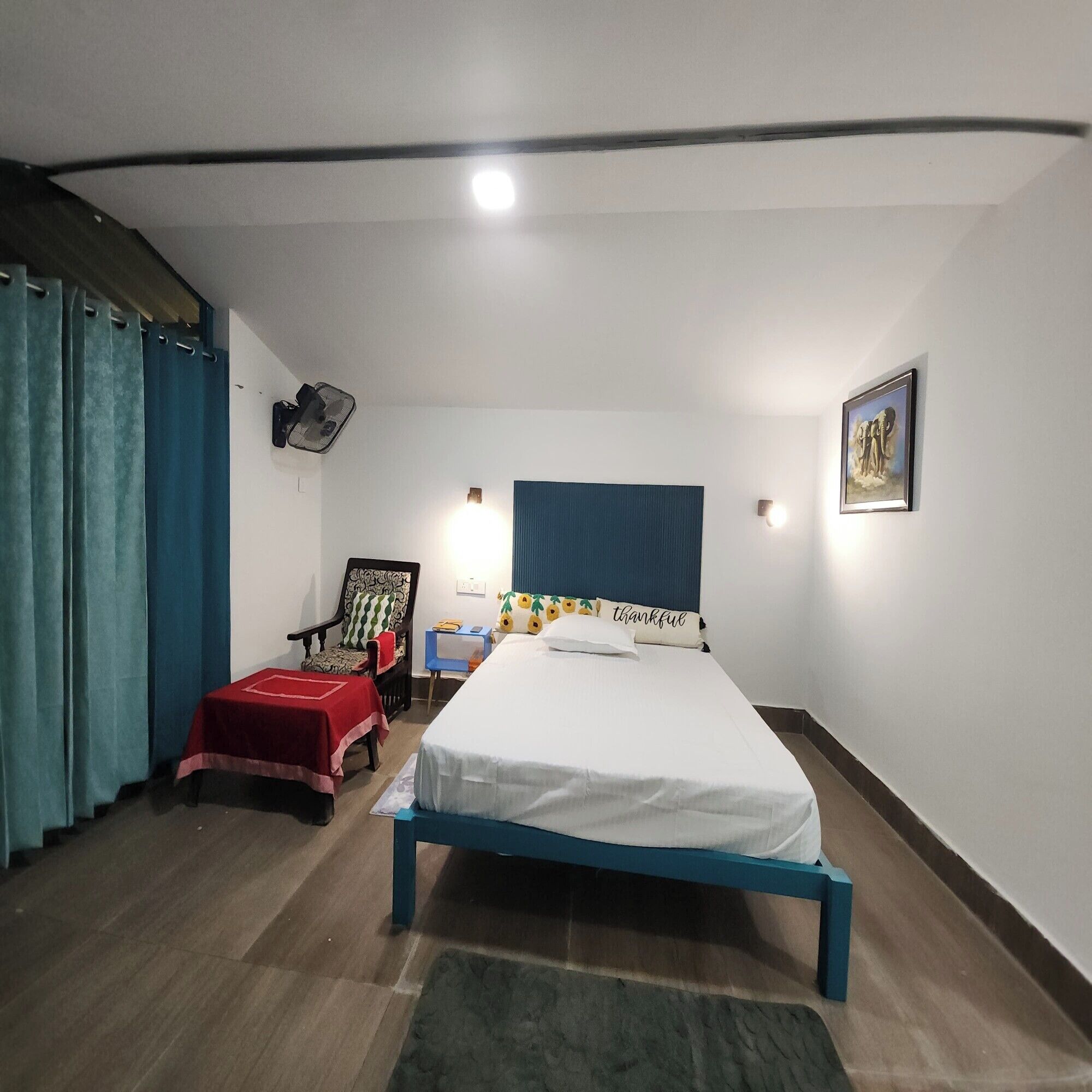 A bedroom with a bed, a chair, a table, and a wall-mounted fan.