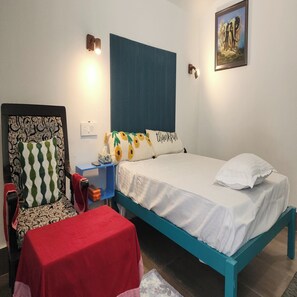 Un dormitorio con una cama, una silla, una mesita y un cuadro en la pared.