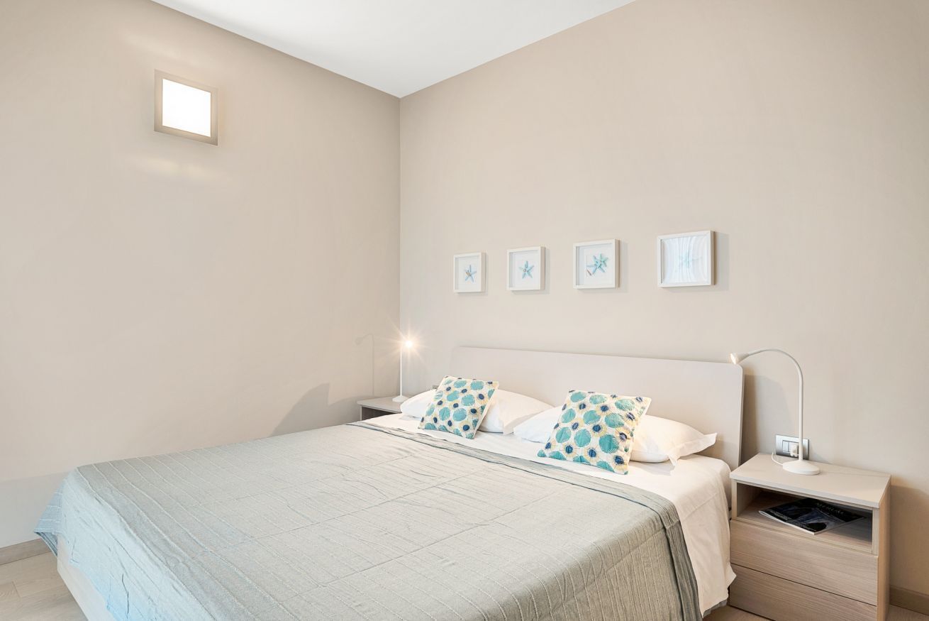 Un dormitorio con cama, mesitas de noche, lámpara de pared y cuadros enmarcados.