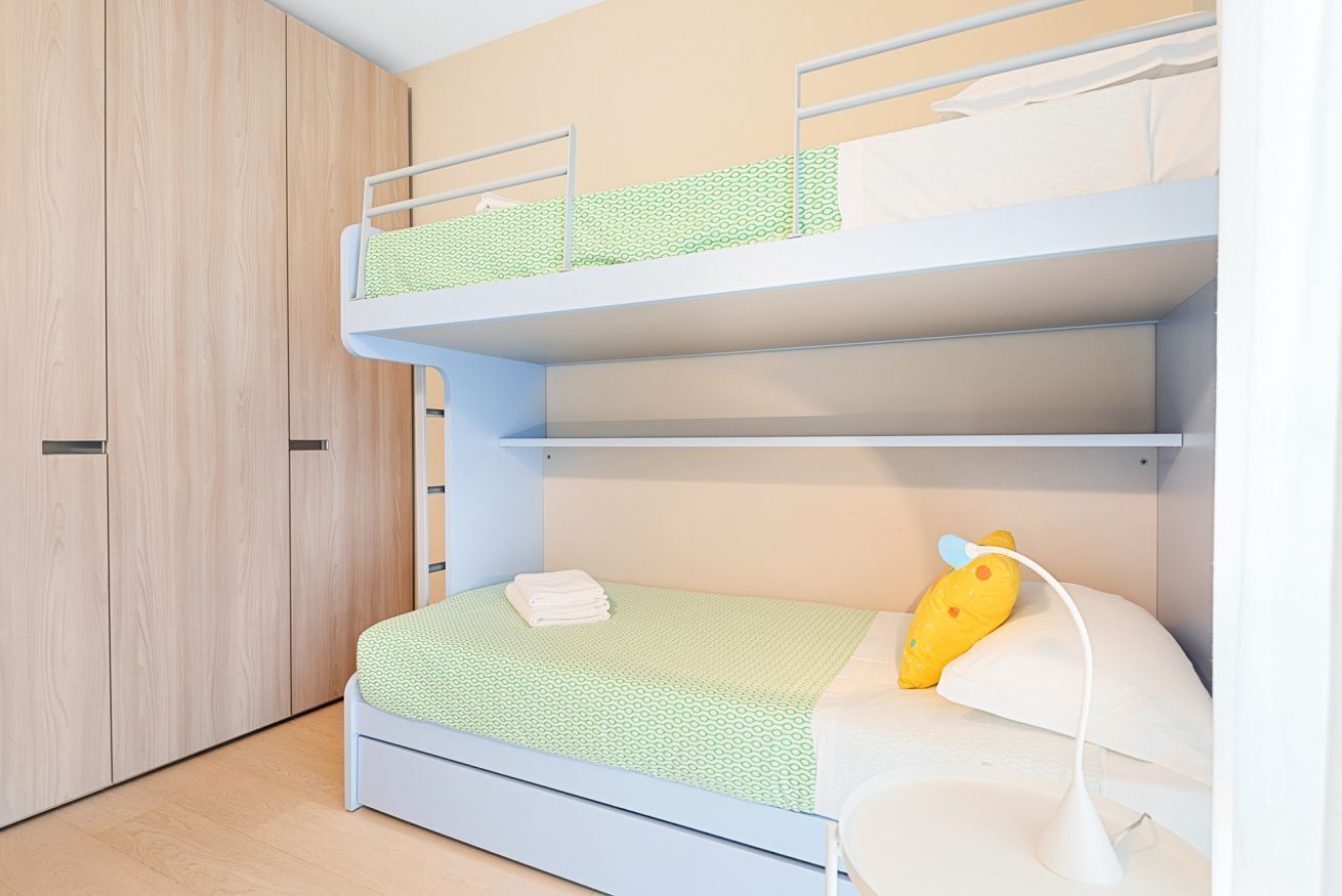 A bunk bed with a green patterned bedspread, a white pillow, and a yellow toy on the lower bunk.