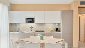 A modern kitchen with white cabinets, a gas stove, and a refrigerator. There is a dining table with chairs and a vase on it. - Levante, amazing modern house in Viareggio city (Viareggio)