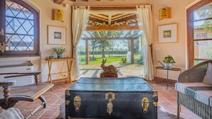 A rustic room with a wooden ceiling, a bench, a wicker chair, a table with a plant, and a view of a garden through a window. - Podere La Troscia is an enchanting Rustic Villa in the Versilia countryside on the Tuscan coast with Garden and Private Pool; the owners love to share this wonderful place with guests from all over the world who intend to visit the North of Tuscany, the  (Piano di Mommio)