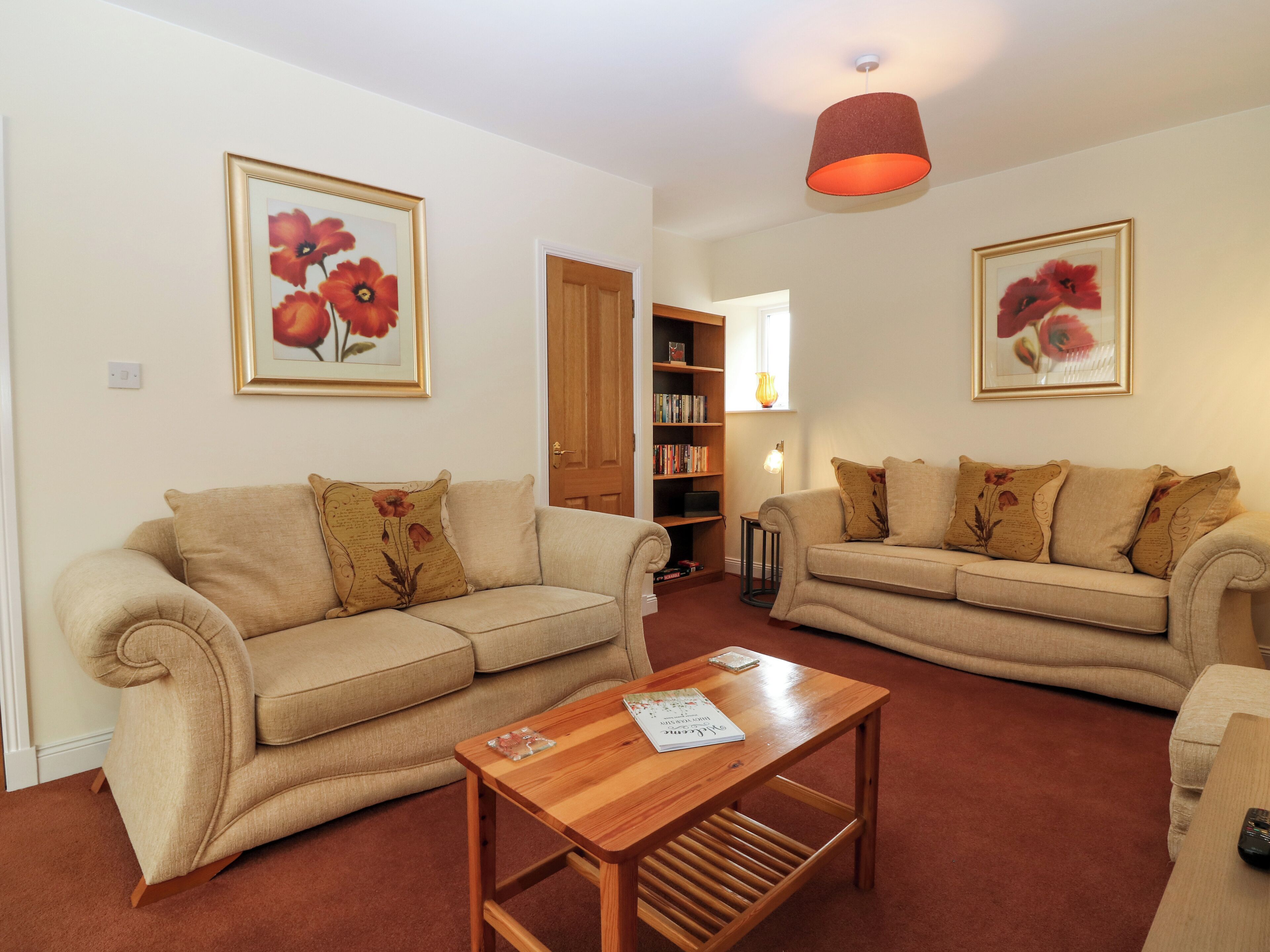 A living room with two beige sofas, a wooden coffee table, and a bookshelf.