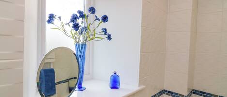 A bathroom with a window, a mirror, a vase with flowers, and a blue soap dispenser.