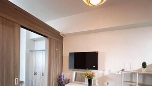 Un dormitorio moderno con cama, televisión montada en la pared, armario y pequeño escritorio con planta.