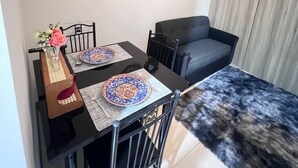 Un espacio habitable pequeño con una mesa de comedor, dos sillas, un sofá y un pequeño espejo decorativo en la pared.
