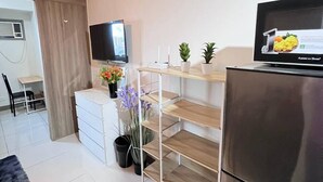 Una cocina moderna con refrigerador de acero inoxidable, estantes de madera, televisor de pantalla plana y un área de comedor con una silla y mesa.