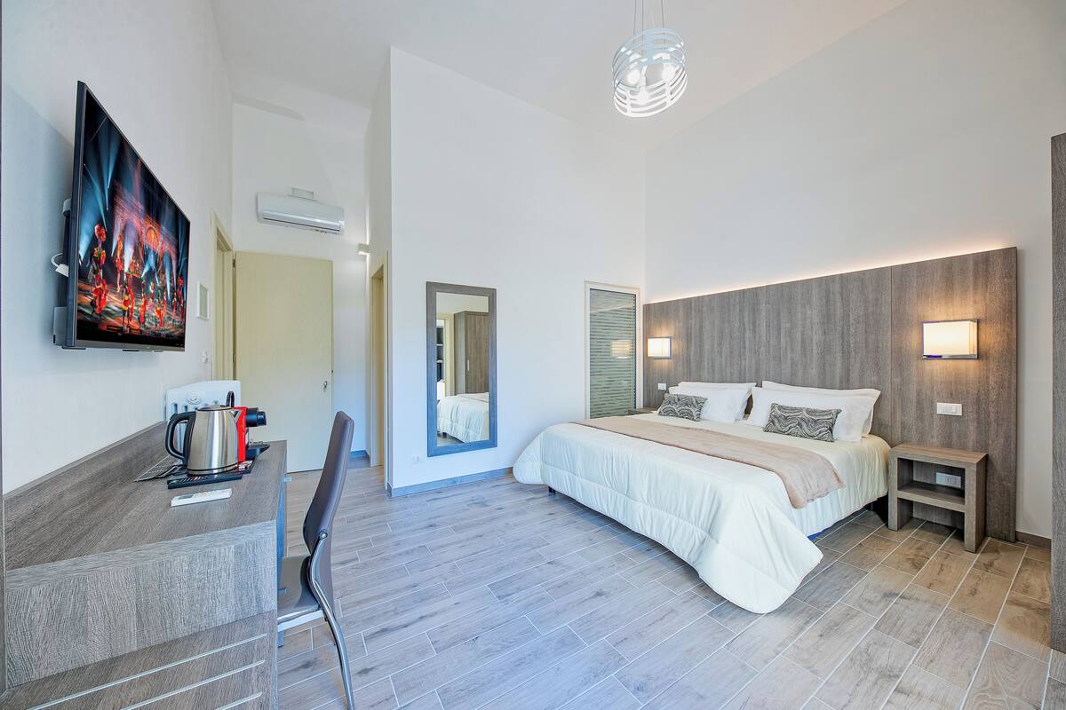 Quarto de hotel moderno com cama, mesa de cabeceira e televisão de tela plana na parede.