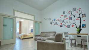 A modern living room with a sofa, a dining table, and a wall decorated with a tree made of pictures. - Hotiday Lecce Gianmarti Suite (Lecce)