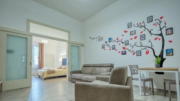 Un salon moderne comprenant un canapé, une table à manger et un mur décoré d’un arbre composé de photographies.