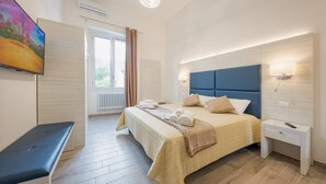 A modern hotel room with a large bed, bedside tables, a bench, and a TV on the wall. - Hotiday Lecce Gianmarti Suite (Lecce)