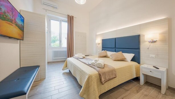 A modern hotel room with a large bed, bedside tables, a bench, and a TV on the wall. - Hotiday Lecce Gianmarti Suite (Lecce)