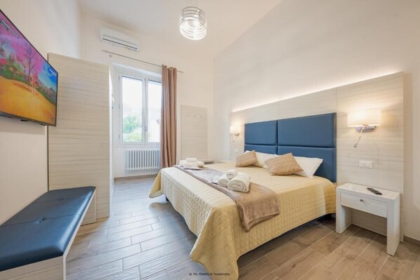 Ein modernes Hotelzimmer mit einem großen Bett, Nachttischen, einer Bank und einem Fernseher an der Wand.