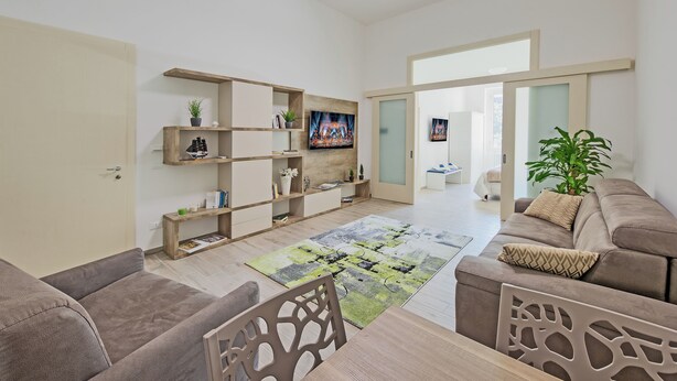 A spacious living room with a large flat-screen TV, wooden shelves, a sofa, and a dining area. - Hotiday Lecce Gianmarti Suite (Lecce)