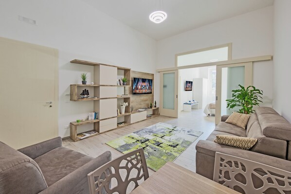 A spacious living room with a large flat-screen TV, wooden shelves, a sofa, and a dining area. - Hotiday Lecce Gianmarti Suite (Lecce)