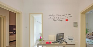 Ein Zimmer mit Schreibtisch, Computer, Drucker und einer Wand mit einem Zitat.