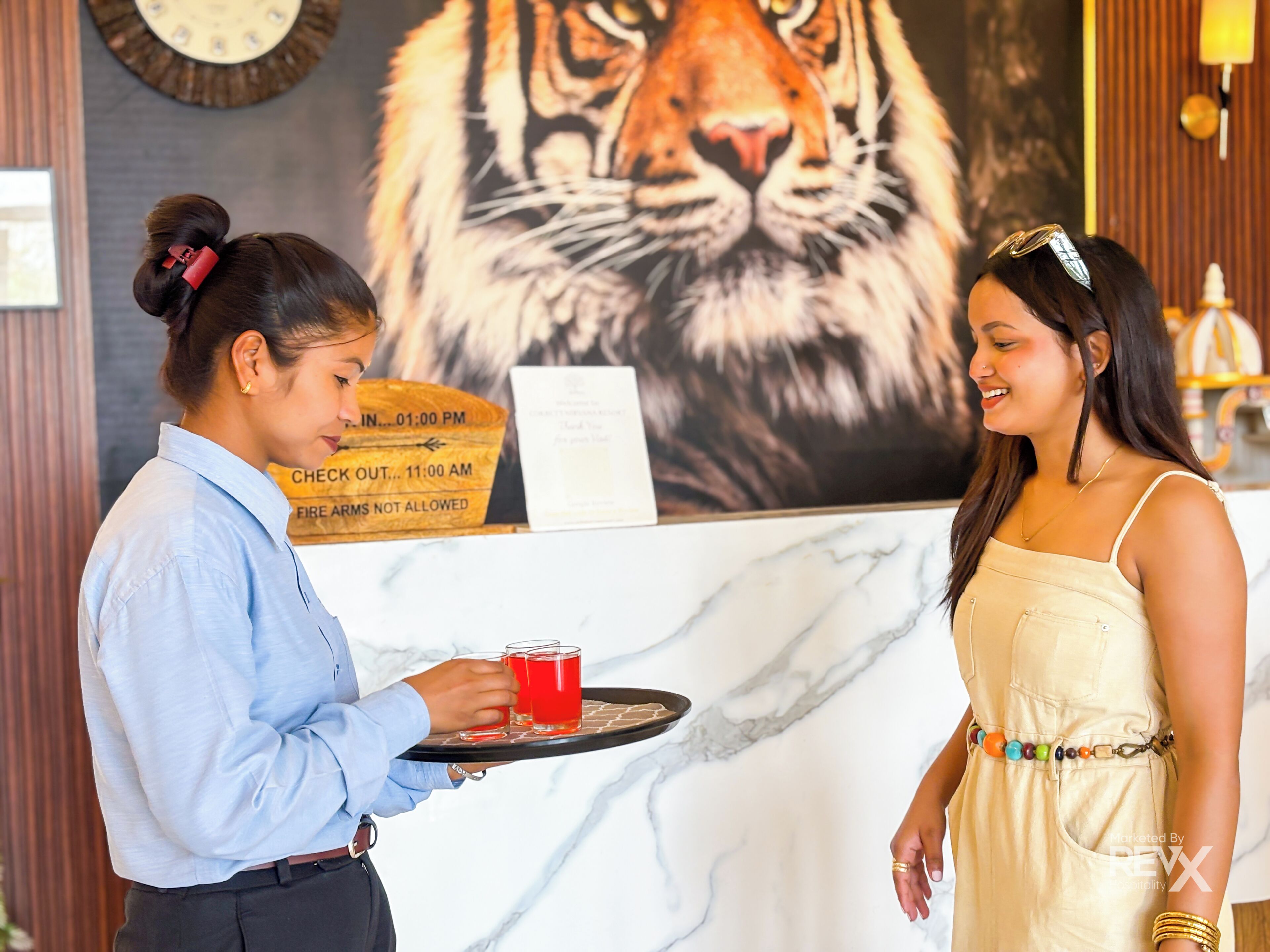 A hotel reception area with a large tiger mural, a clock, and a sign indicating check-out times.