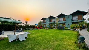 A courtyard with a grassy lawn, outdoor furniture, a children's play area, and a building with balconies. - CORBETT NIRVANA RESORT (Ramnagar)