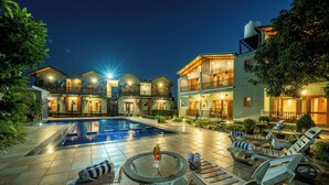 A pool area with lounge chairs and a table, surrounded by buildings with balconies and a water tank on the roof. - CORBETT NIRVANA RESORT (Ramnagar)