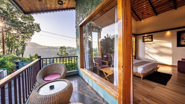 A balcony with wicker furniture, a bed with a wooden frame, and a view of the landscape. - CORBETT NIRVANA RESORT (Ramnagar)