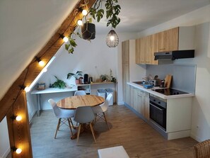 A modern kitchen with wooden cabinets, a built-in oven, and a dining area with a round wooden table and chairs. - "Le 105" in Larmor-Plage, garden view, parking and cellar (Larmor-Plage)